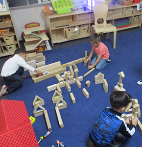 Three students playing with blocks on a classroom floor