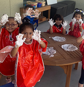 Group of students wearing smocks hold up their hands covered in whipped cream